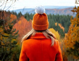 Woman wearing an orange coat and orange woolly hat looking at a view of an autumn forest