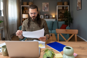 Young worried, confused and stressed overworked freelance business man working at home office looking statistics and results of research and calculations. Businessperson search for mistake he made.