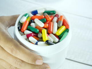 Hand holding a white can containing many capsules of antibiotics.