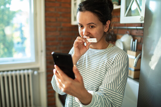 Woman showing positive pregnancy test to smartphone at home