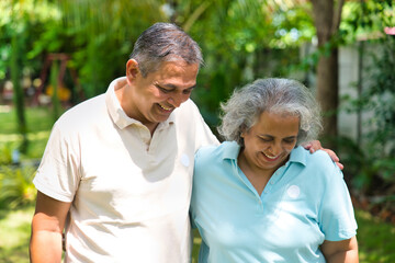 Indian couple in their fifties walking in the park, smiling and discussing with gestures