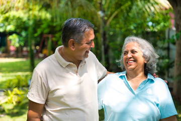 Indian couple in their fifties walking in the park, smiling and discussing with gestures