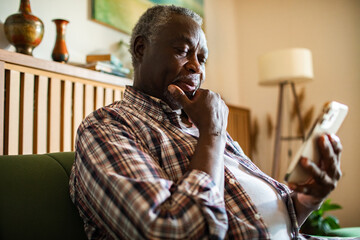 Senior man using smartphone on the couch at home