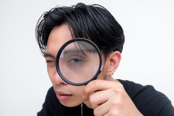 A curious young asian man bending down and intently looking at something with a magnifying glass....