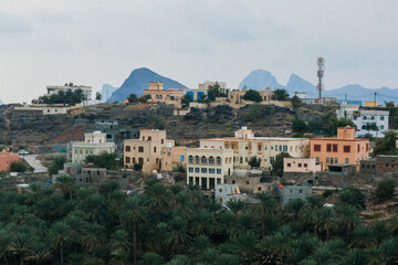 Naklejka premium A tranquil village in Oman nestled among hills and palm trees under a cloudy sky