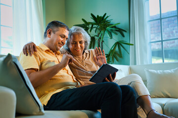 Obraz premium Indian couple in their fifties making a video call on a smartphone or laptop, near sunny window