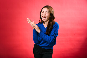 An Asian woman in a blue sweater, clapping her hands with a cheerful expression, standing against a red background. Her joyful energy and excitement are vividly displayed.