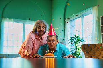 Husband's birthday celebration with cake and clapping wife in cozy home setting filled with joy