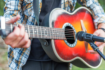 Obraz premium Male hands with an acoustic guitar against a background of a country landscape.