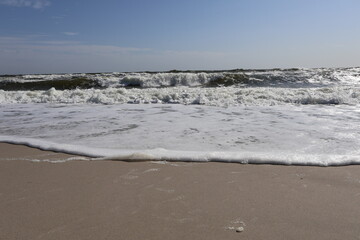 Foamy Ocean Waves Gently Reaching Sandy Shore on a Clear Day