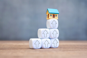 A miniature house on top of a white blocks with upward arrows. Housing market, price growth and...