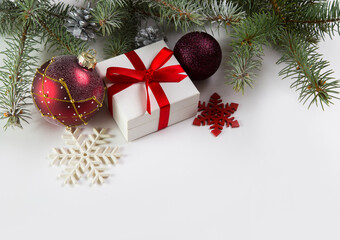 A white box with a gift tied with a red ribbon, a spruce branch and obligatory decorations on a white background