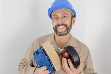 portrait of mature builder holding sander and earmuffs