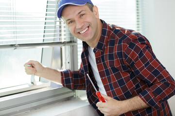 construction worker adjusting installed window with screwdriver indoors