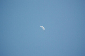 A clear image of a crescent moon visible during the daytime against a vibrant blue sky, highlighting a serene natural phenomenon.