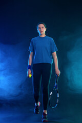 Tennis player woman with racket on tournament. Girl athlete with racket on open court with blue neon colors. Full height photo.