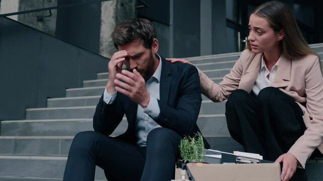 Caucasian stressed male man guy with box sitting on stairs of office businessman dismissed from work business dismiss unemployment woman female girl businesswoman friend support calm console in city