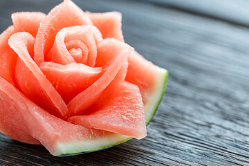 a delicate watermelon rose carving with precise details, dark wooden surface