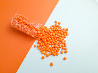 Orange masterbatch granules spill out of a glass tube on a white and orange background.Color pigment carrier polymer in the plastics industry.