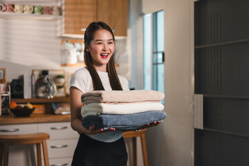 young woman smiles while holding neatly stacked towels in modern kitchen. warm lighting and cozy setting create welcoming atmosphere, perfect for home comfort