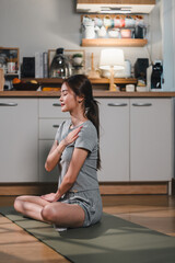 Mindful woman practicing yoga in cozy kitchen, promoting relaxation and wellness. She sits gracefully on mat, embodying tranquility and focus
