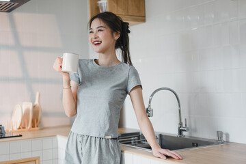 woman in gray outfit smiles while holding mug in modern kitchen, radiating joy and comfort. bright...
