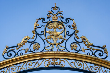 Detail of ancient golden decor with crocodile and palm tree - coat of arms of the city - on top of fence of Jardins de la Fontaine, Nîmes, Gard, France	

