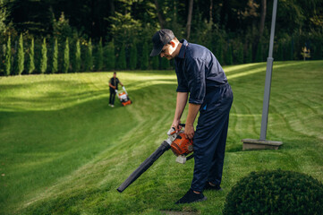 Standing and using leaf blower. Professional gardener is on the lawn