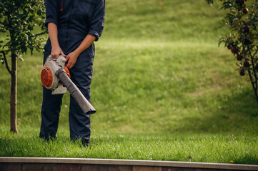 Leaf blower in hands, cleaning the way. Professional gardener is on the lawn