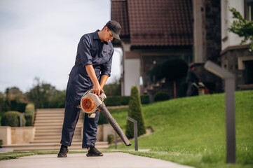 Leaf blower in hands, cleaning the way. Professional gardener is on the lawn