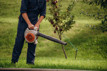 Leaf blower in hands, cleaning the way. Professional gardener is on the lawn