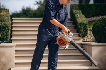 At sunny daytime, using leaf blower. Professional gardener is on the lawn