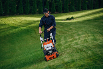 Process of cutting the grass by using lawn mover. Professional gardener is on the lawn