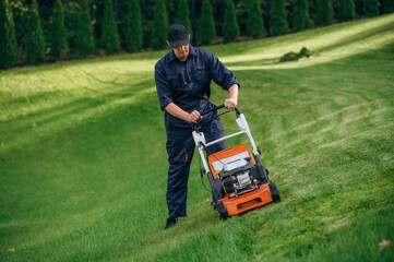 Process of cutting the grass by using lawn mover. Professional gardener is on the lawn