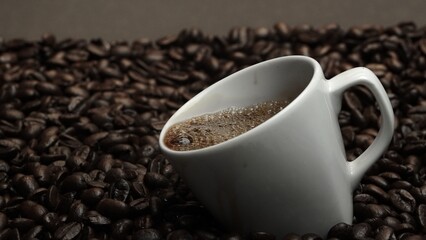 Close up of coffee bean falling in to coffee cup surrounded by pile of beans. Dropping aromatic blending bean in to white cup. Top view of coffee drop in to glass with black background. Comestible.