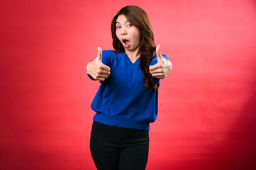 An asian cheerful woman wearing a blue sweater and black pants smiles while giving two enthusiastic...