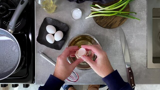 Top view of man breaking chicken eggs to make omelette in the morning in home kitchen.