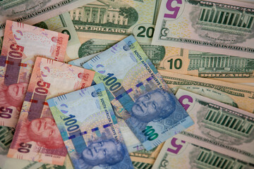 Selective focus on R50 and R100 South African currency notes with various denominations of US Dollar notes behind them. 