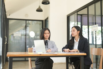  Two professional business executives working on laptop computer sitting at office desk, happy colleagues discussing company digital strategy.