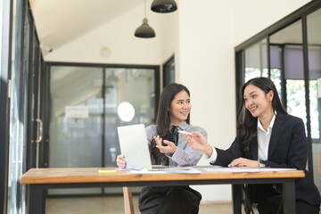  Two professional business executives working on laptop computer sitting at office desk, happy colleagues discussing company digital strategy.