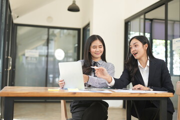 Happy Asian business people working together using laptop and tablet in office.