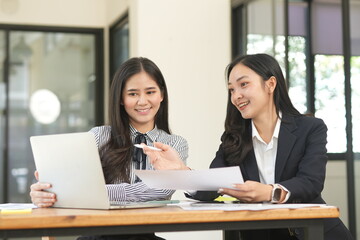  Two professional business executives working on laptop computer sitting at office desk, happy colleagues discussing company digital strategy.