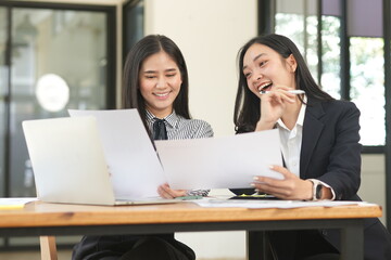 Happy Asian business people working together using laptop and tablet in office.