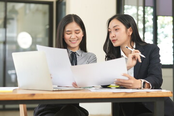  Group of happy Asian business people having a meeting at the office. Two women working together using modern laptops.
