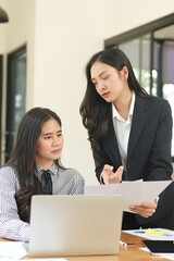  Group of happy Asian business people having a meeting at the office. Two women working together using modern laptops.