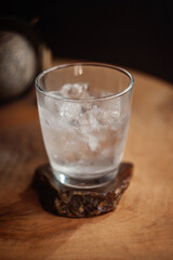 A glass of iced water, vodka, tonic, club soda on the rocks on a wooden table