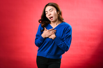 An Asian woman in a blue sweater clutches her chest in apparent distress, as if experiencing sudden...
