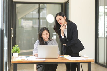 Happy Asian business people working together using laptop and tablet in office.