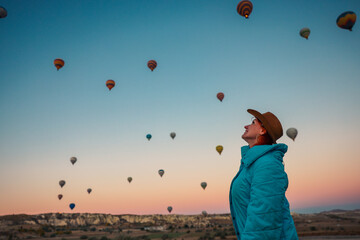 A woman marvels at colorful hot air balloons floating above Cappadocia at dawn capturing the enchanting beauty of the landscape