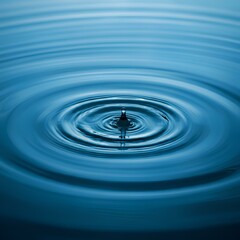 A water droplet creates ripples in a calm blue surface, forming circular waves in the water.